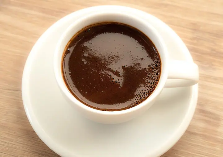 Šoljica kafe na tanjiriću, fotografisana odozgo na drvenom stolu