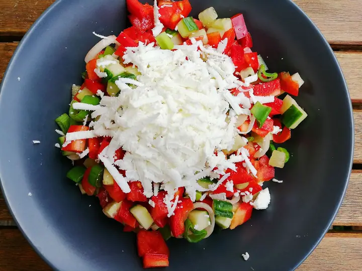 Zdjela šopske salate od paradajza, krastavca, paprike i luka, posuta rendanim sirom