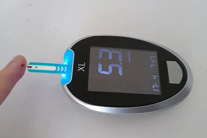 Glukometar s test trakom na koju je nanesena kap krvi s prsta, na ekranu 5,3
